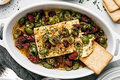 a white bowl filled with vegetables and fish next to crackers on a table top