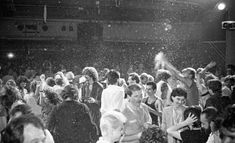 a crowd of people standing around each other in front of a stage with confetti falling from the ceiling