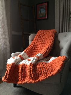 an orange and white crocheted blanket sitting on top of a chair in front of a window