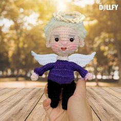 a hand holding a small crocheted angel doll on top of a wooden table