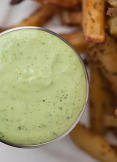 a glass filled with green liquid next to some fries