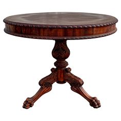 a round wooden table with ornate carvings on the top and bottom, sitting against a white background