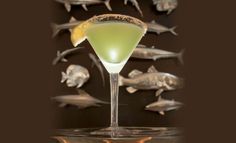 a martini glass filled with green liquid surrounded by fish