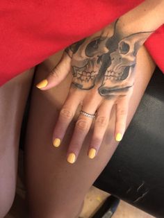 a woman's hand with a skull tattoo on her left arm and yellow nails