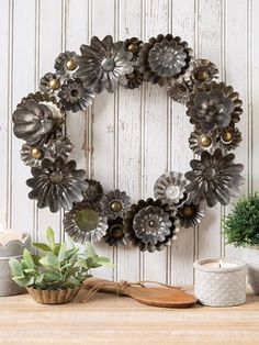 a wreath made out of metal flowers sitting on top of a wooden table next to a potted plant