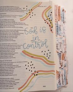 an open bible with the words god is in control written on it and colorful lines