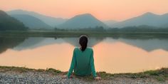 a person sitting on the ground looking out over a lake