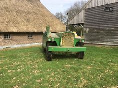 a green tractor parked in front of a thatched roof house with grass on the lawn