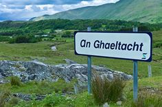 a sign that is in the grass near some rocks and trees with mountains in the background