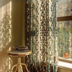 the sun is shining through the curtains in this room with a small table and chair