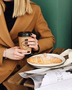 a woman sitting at a table with a coffee cup and croissant in front of her