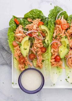 two lettuce wraps filled with chicken, tomatoes and avocado on a white plate