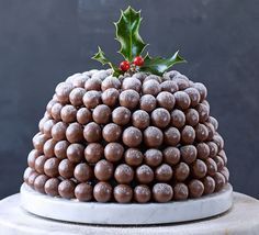 a christmas cake decorated with chocolate balls, holly and mistlet leaves on a white pedestal