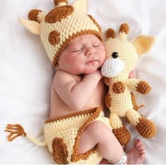 a baby wearing a crocheted giraffe outfit and holding a stuffed animal