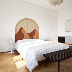 a bedroom with a large bed and wooden flooring in front of a painting on the wall