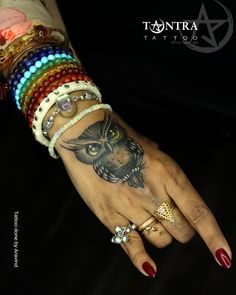 a woman's hand with many bracelets on it and an owl tattoo on the wrist