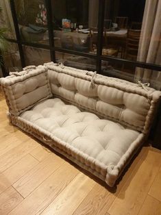 a white couch sitting on top of a hard wood floor next to a window with curtains