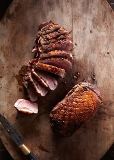 sliced meat sitting on top of a wooden cutting board next to a knife and fork