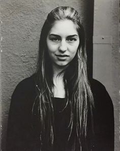 an old black and white photo of a woman with long hair in front of a wall