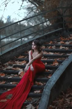 a woman in a red dress is sitting on some stairs with leaves all over her