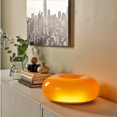 an orange light sitting on top of a white counter next to a vase and books