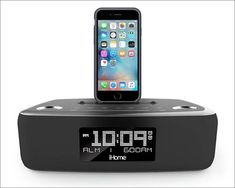 an alarm clock and cell phone are on top of the speaker system that is charging