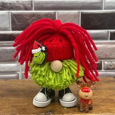 a red and green knitted troll doll next to a small toy dog on a wooden table