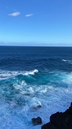 the ocean is blue and foamy with waves coming in from the rocks on the shore