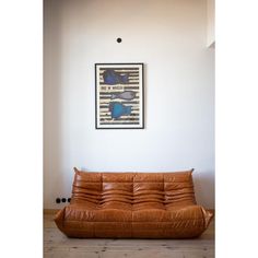 a brown leather futon is in front of a white wall with a framed poster on it