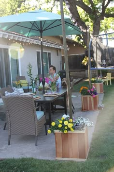 a woman sitting at a table with an umbrella over her head and potted flowers in front of her