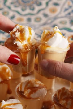 a hand is holding two small cups with ice cream and caramel sauce on them