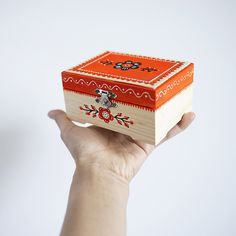 a hand holding a small wooden box with an orange and red design on the lid