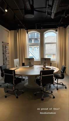 a round table with chairs around it in front of two windows