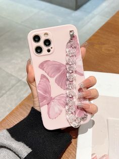 a person holding a pink phone case with butterflies on it and some beads hanging from the back