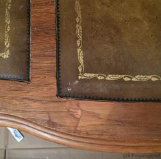 an old wooden table with two brown leather seats on it's sides and gold trim around the edges