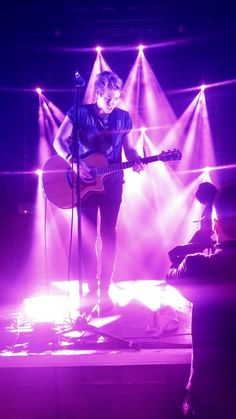 a man standing on top of a stage holding a guitar