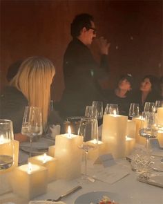 people are sitting at a table with candles on it and wine glasses in front of them