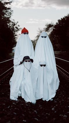 two people dressed in white standing on train tracks with their heads covered by coverings