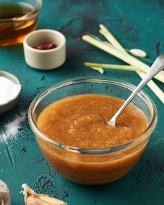 a glass bowl filled with peanut butter next to garlic and other ingredients on a blue surface