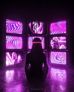 a person sitting on the floor in front of tvs with different colored images behind them