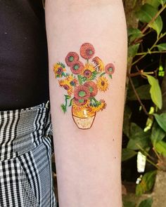 a woman with a tattoo on her arm holding a vase of sunflowers in it