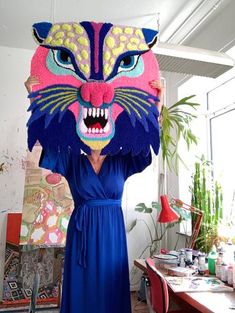 a woman in a blue dress holding up a paper mask with a cat's face on it