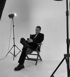 a black and white photo of a man sitting on a chair in front of a camera