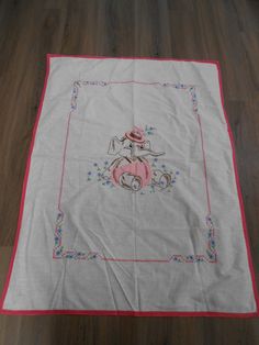 a white table cloth with a pink border and an elephant on the front, sitting on top of a wooden floor