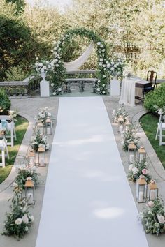 an outdoor ceremony setup with white flowers and greenery on the aisle, surrounded by chairs