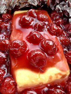 a piece of cheesecake covered in cherries on top of tin foil with syrup