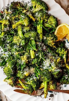 a white plate topped with broccoli covered in parmesan cheese and lemon wedges