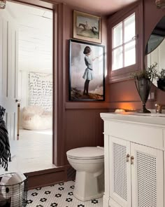 a white toilet sitting in a bathroom next to a painting on the side of a wall