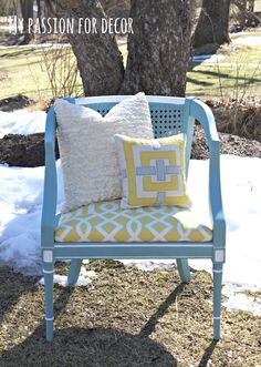 a blue chair sitting in front of a tree with two pillows on top of it