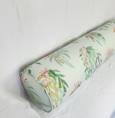 a rolled up pillow sitting on top of a white sheeted bed covered in green and pink flowers